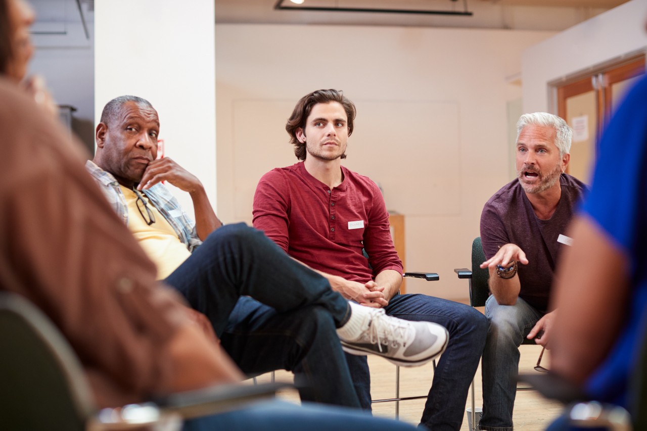 Eine Gruppe Männer sitzt in einem Stuhkreis und diskutiert angeregt über ein Thema
