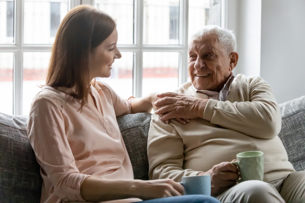 Junge Frau und älterer Mann lachend auf einem Sofa